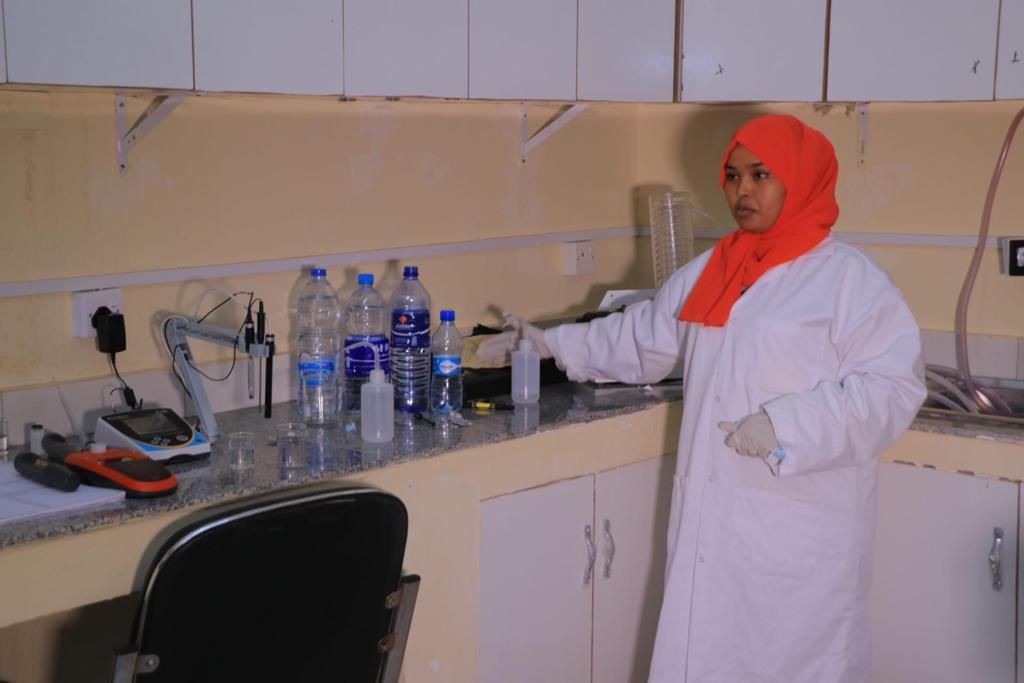 Person in a lab coat working with plastic bottles and lab equipment on a countertop.