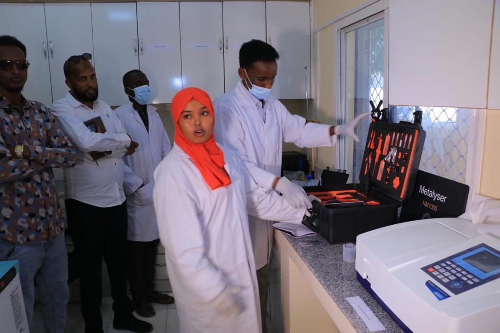 Laboratory technician explaining equipment to colleagues, with lab tools in an open case on the counter.